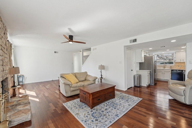 living room with ceiling fan, visible vents, a fireplace, and dark wood-style flooring