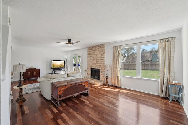 living room featuring baseboards, ceiling fan, a stone fireplace, wood finished floors, and a textured ceiling