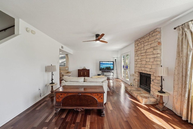 living room featuring visible vents, baseboards, a stone fireplace, wood finished floors, and a ceiling fan