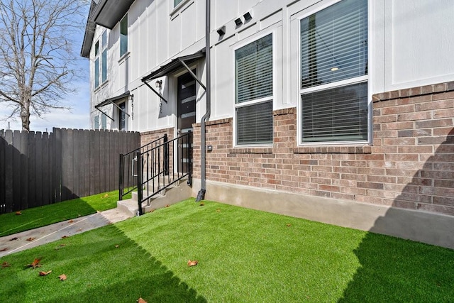 view of property exterior featuring brick siding, a lawn, and fence