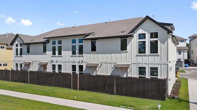 back of property with a fenced front yard, a residential view, a lawn, and board and batten siding