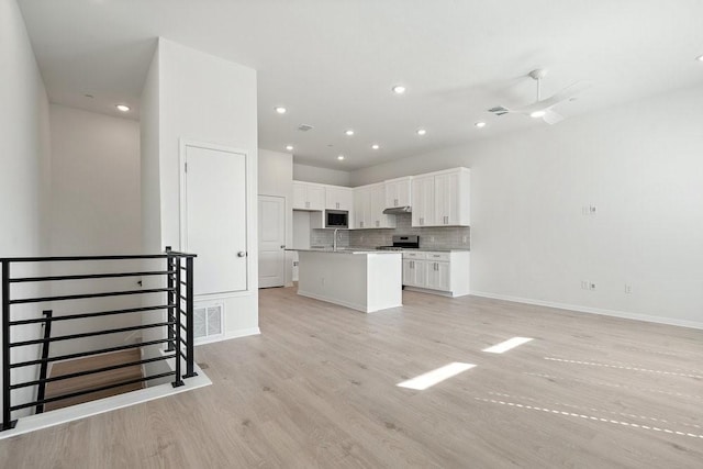 kitchen featuring open floor plan, backsplash, stainless steel appliances, and light wood-type flooring