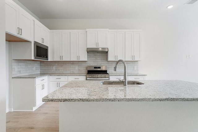 kitchen with light wood-style flooring, a sink, under cabinet range hood, appliances with stainless steel finishes, and white cabinetry