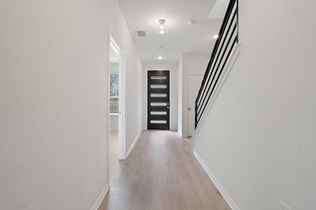 hallway featuring visible vents, stairs, light wood-type flooring, and baseboards