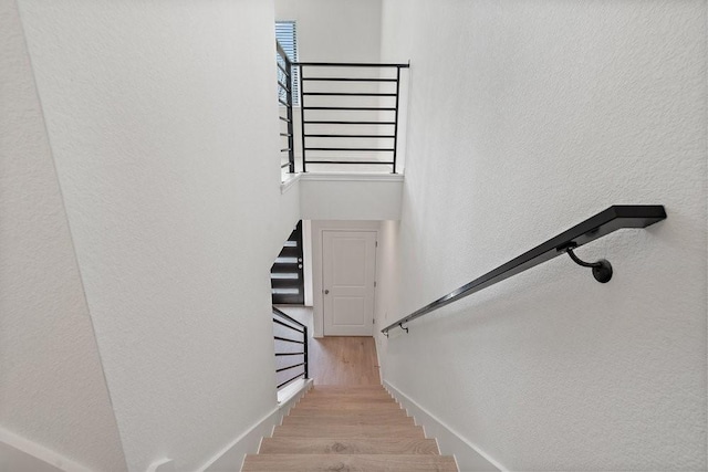 staircase featuring a towering ceiling, wood finished floors, and a wealth of natural light