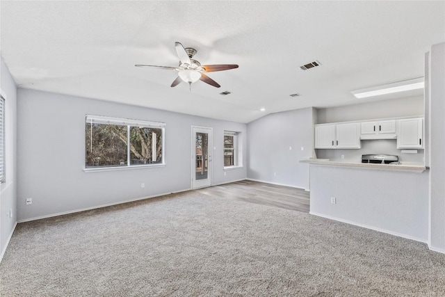 unfurnished living room featuring a ceiling fan, visible vents, baseboards, vaulted ceiling, and light colored carpet