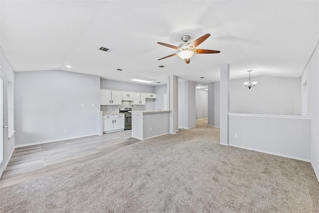 unfurnished living room with visible vents, baseboards, vaulted ceiling, light carpet, and ceiling fan with notable chandelier