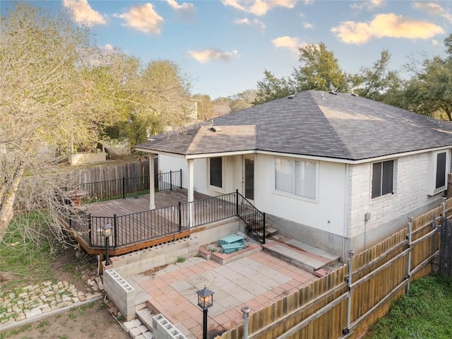 rear view of house featuring fence, a shingled roof, a deck, a patio area, and brick siding