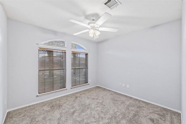 carpeted spare room with visible vents, baseboards, and a ceiling fan