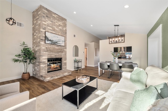 living room with a high ceiling, a brick fireplace, wood finished floors, and visible vents