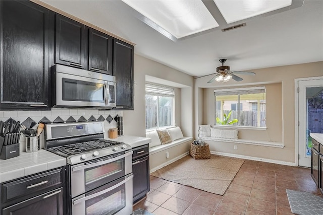 kitchen featuring dark cabinetry, tile countertops, visible vents, appliances with stainless steel finishes, and tasteful backsplash