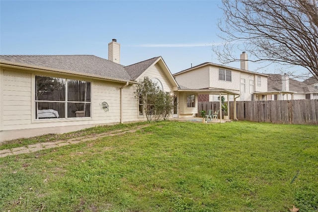 rear view of property with a lawn, fence, roof with shingles, a chimney, and a patio area