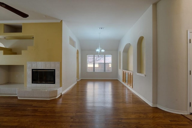 unfurnished living room featuring visible vents, wood finished floors, an inviting chandelier, a fireplace, and baseboards