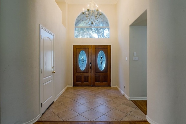 entryway with light tile patterned floors, baseboards, an inviting chandelier, and a towering ceiling