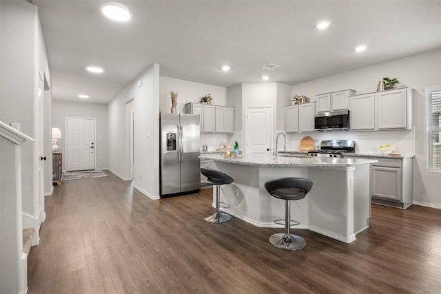 kitchen featuring a kitchen bar, stainless steel appliances, dark wood-type flooring, and an island with sink