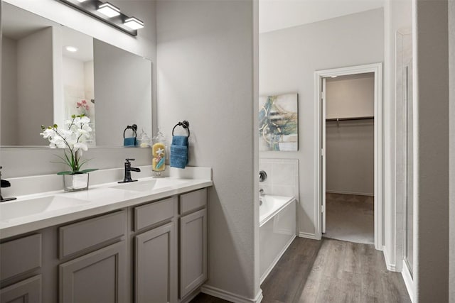 full bath with a garden tub, wood finished floors, double vanity, and a sink