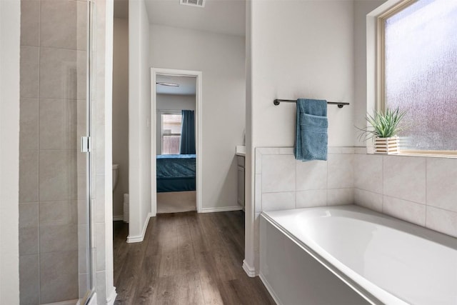 bathroom with visible vents, a garden tub, wood finished floors, a shower stall, and baseboards