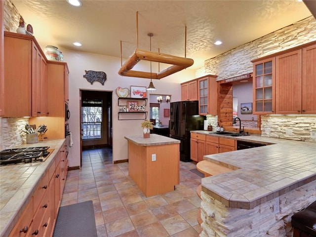 kitchen featuring tasteful backsplash, a kitchen island, black refrigerator with ice dispenser, gas cooktop, and a sink