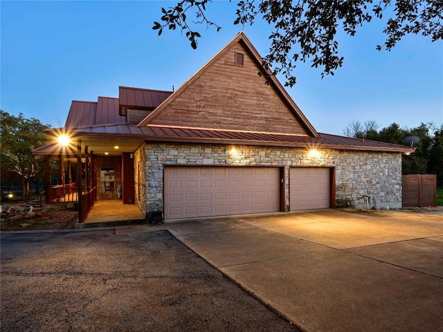 view of front of property with driveway, a standing seam roof, stone siding, a garage, and metal roof