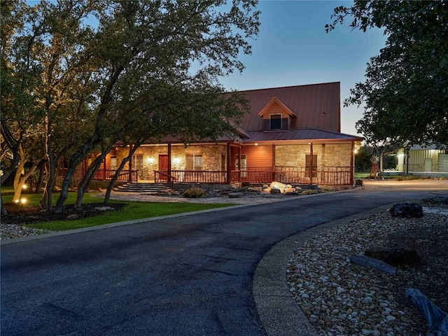 view of front facade featuring metal roof, stone siding, covered porch, and driveway