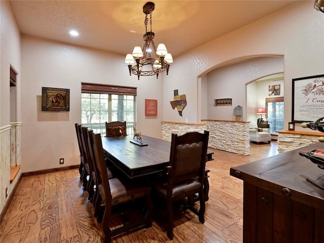 dining area with a chandelier, baseboards, arched walkways, and light wood-style flooring