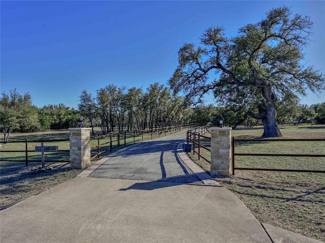 view of road featuring a rural view, concrete driveway, a gated entry, and a gate