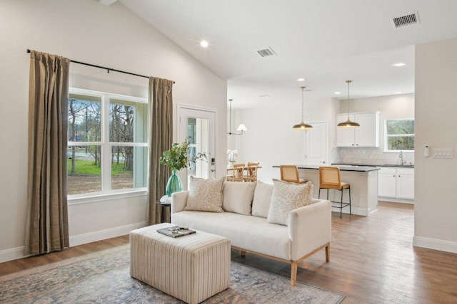 living area with vaulted ceiling, baseboards, visible vents, and light wood finished floors