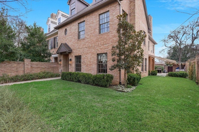 view of home's exterior with fence, a lawn, and brick siding