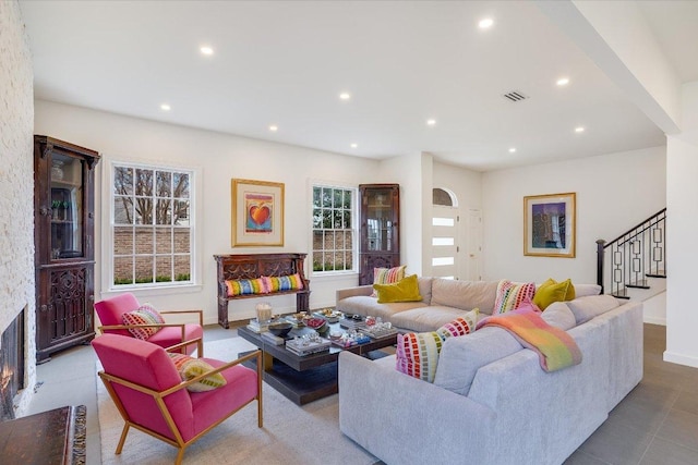 living area with a stone fireplace, plenty of natural light, recessed lighting, and stairs