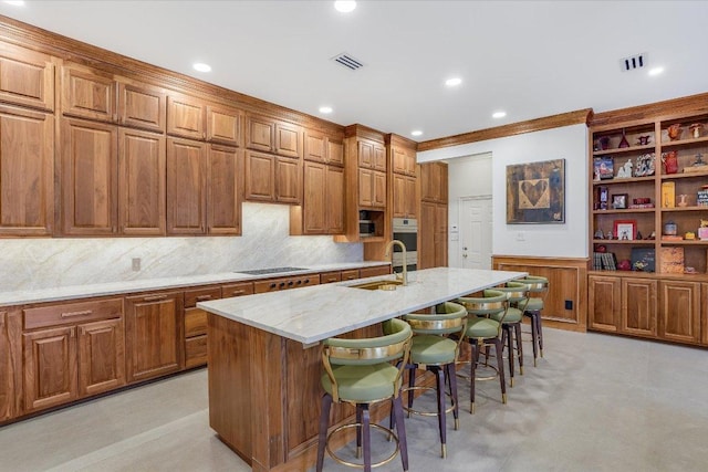 kitchen featuring a sink, black electric stovetop, a kitchen bar, light stone counters, and a kitchen island with sink