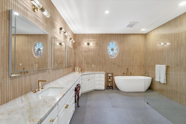 bathroom with visible vents, a sink, tile walls, double vanity, and a soaking tub