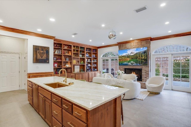 kitchen featuring a sink, a brick fireplace, a healthy amount of sunlight, and an island with sink