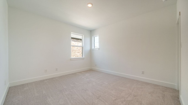 spare room with baseboards and light colored carpet