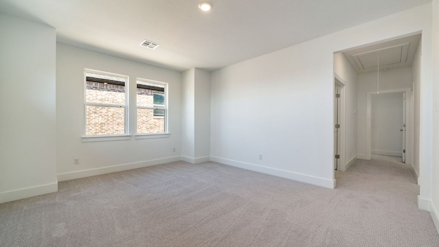 spare room featuring light carpet, visible vents, attic access, and baseboards