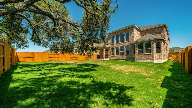 back of house featuring brick siding, a lawn, and a fenced backyard