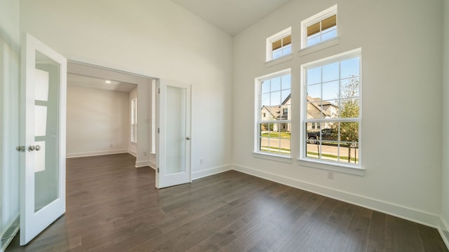 spare room featuring french doors, baseboards, a high ceiling, and dark wood finished floors