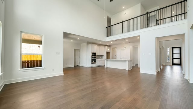 unfurnished living room with recessed lighting, baseboards, dark wood-style flooring, and a sink