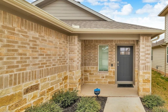 doorway to property with stone siding, brick siding, and roof with shingles