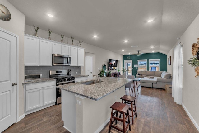 kitchen with a sink, a breakfast bar area, decorative backsplash, appliances with stainless steel finishes, and dark wood-style flooring