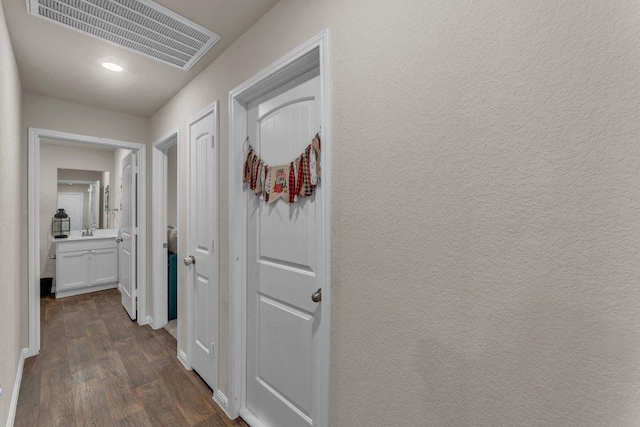 hall with visible vents, a sink, dark wood finished floors, baseboards, and a textured wall