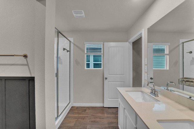 full bath with wood finished floors, baseboards, double vanity, a stall shower, and a sink