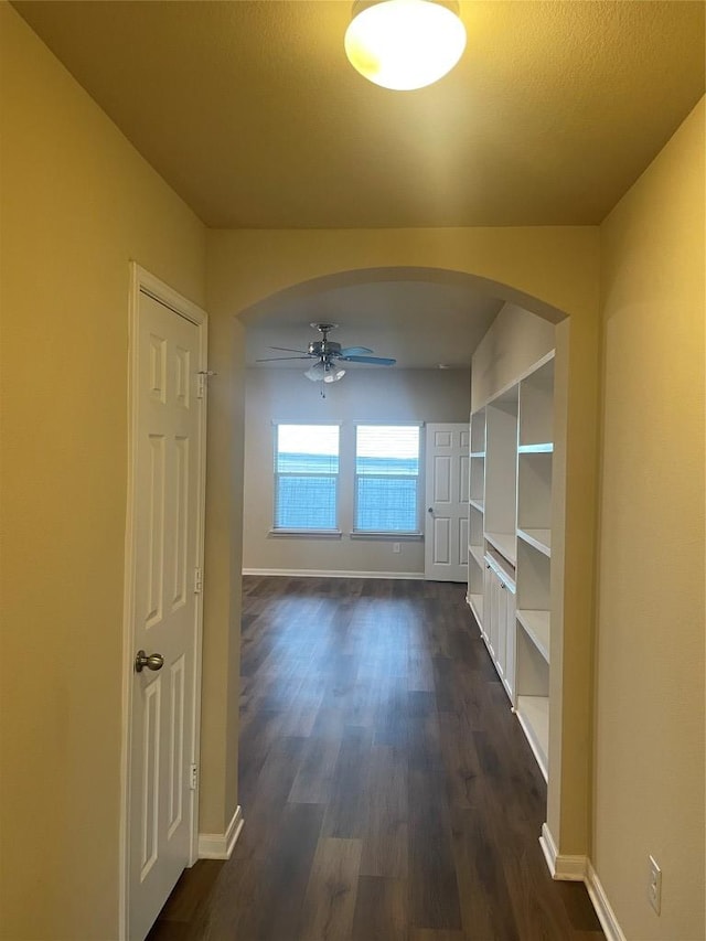 hall with dark wood-type flooring, baseboards, and arched walkways