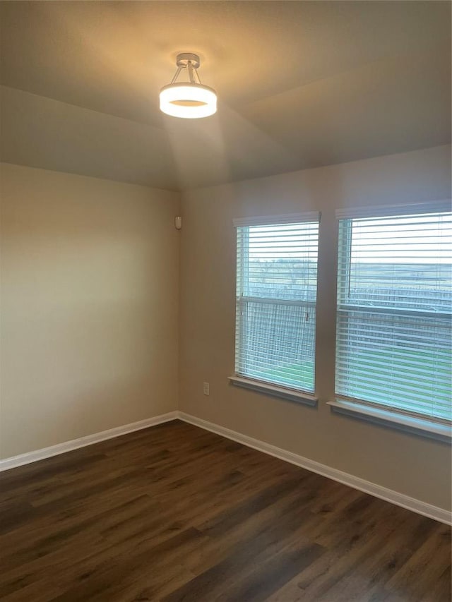 empty room with dark wood-type flooring, lofted ceiling, and baseboards