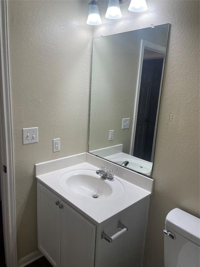 bathroom with toilet, vanity, and a textured wall