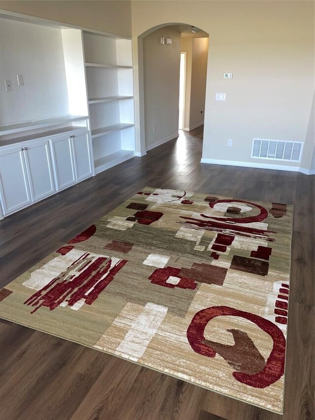 empty room featuring wood finished floors, arched walkways, and visible vents