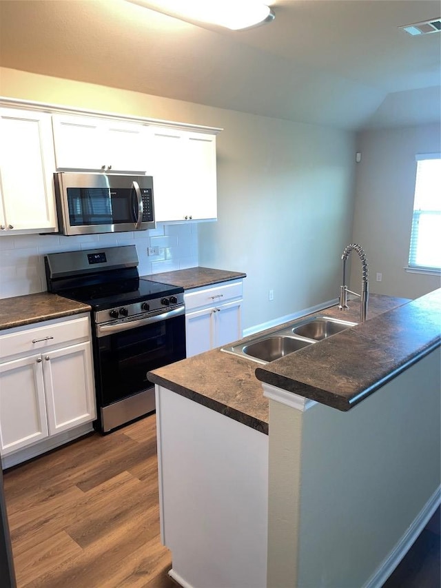 kitchen featuring white cabinetry, wood finished floors, stainless steel appliances, and dark countertops