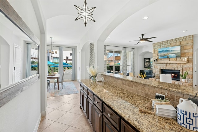 kitchen featuring a large fireplace, baseboards, decorative light fixtures, light stone counters, and light tile patterned floors