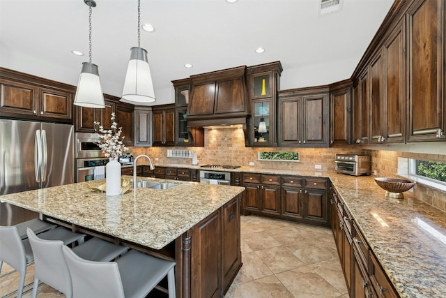 kitchen featuring a breakfast bar area, premium range hood, a sink, decorative backsplash, and stainless steel appliances