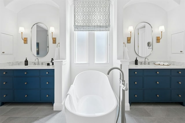 bathroom featuring a sink, a freestanding bath, two vanities, and tile patterned floors