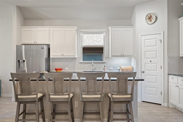 kitchen featuring light wood-style flooring, a sink, white cabinetry, stainless steel fridge, and backsplash